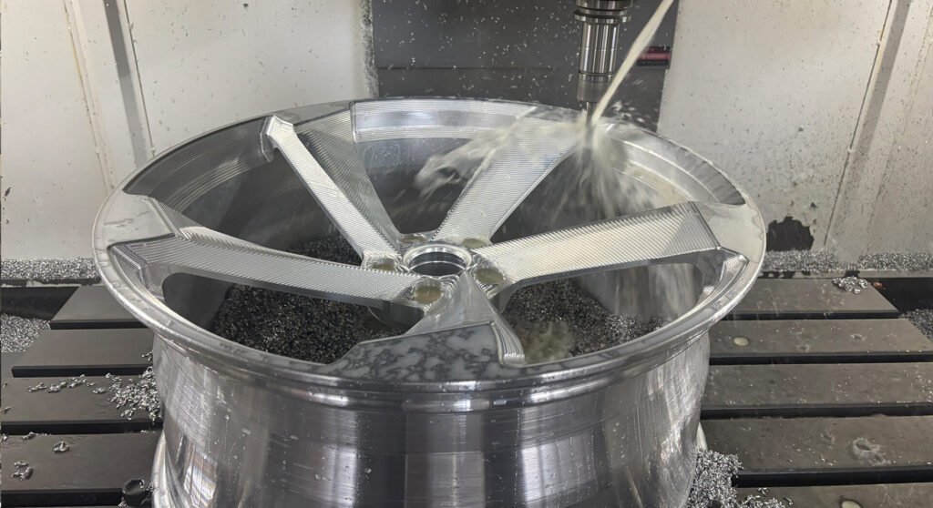 CNC machine precision milling a forged wheel face with coolant spray