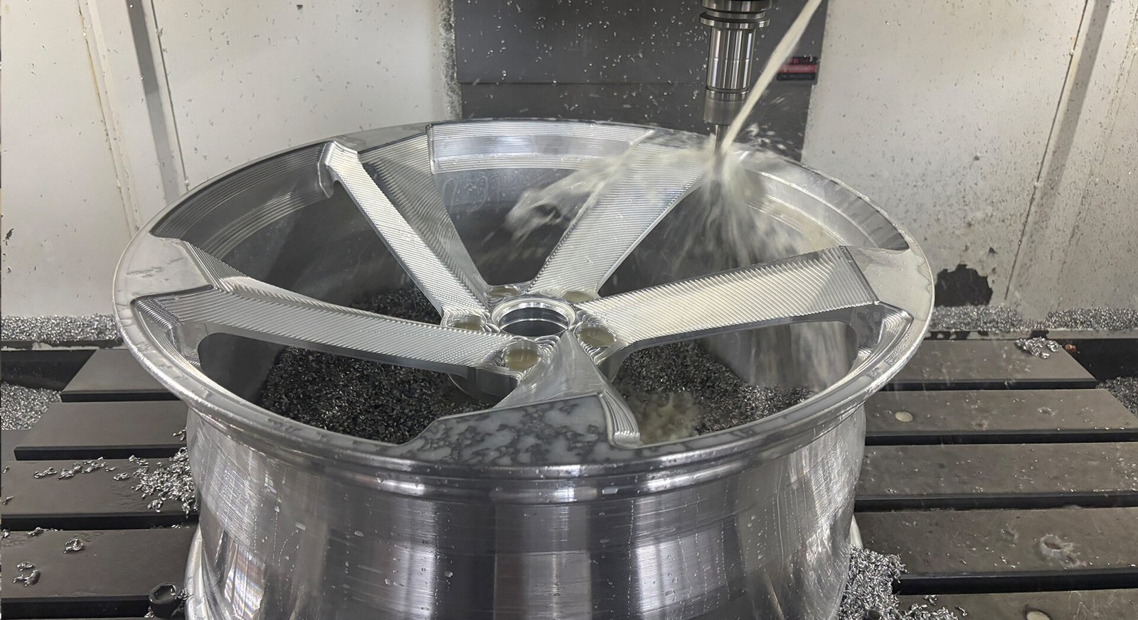 CNC machine precision milling a forged wheel face with coolant spray
