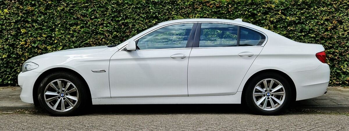 White BMW 5 Series F10 sedan, side view showing factory alloy wheels