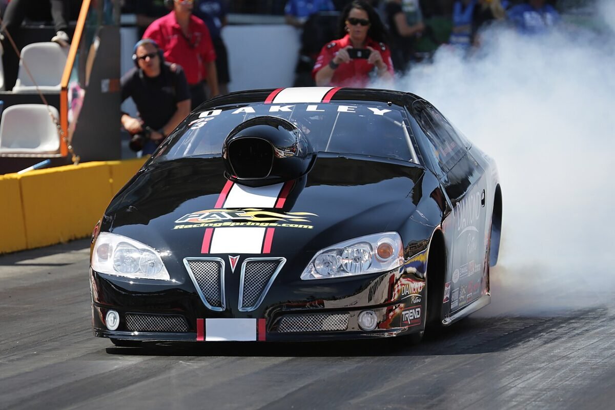 Pro Stock drag car doing a burnout on 15-inch rear drag wheels, showing the wide rear wheel tucked under the quarter panel